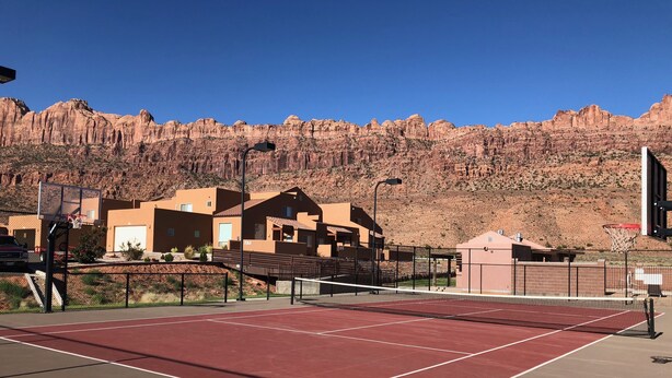 Ein Tennisplatz mit roter Belag, umgeben von Gebäuden und einer Bergkulisse.