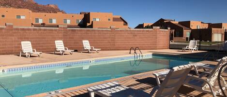 A pool area with lounge chairs, a clear pool, and a brick wall.