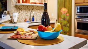 A kitchen counter with a blue bowl containing fruits and a bottle of wine, a cutting board with sliced meats, and a decorative cactus plant. - Tequila Sunrise, Large Pool Home (Lake Havasu City)