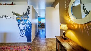 A hallway with a welcome sign, a mirror, a lamp, and a patterned rug. - Tequila Sunrise, Large Pool Home (Lake Havasu City)