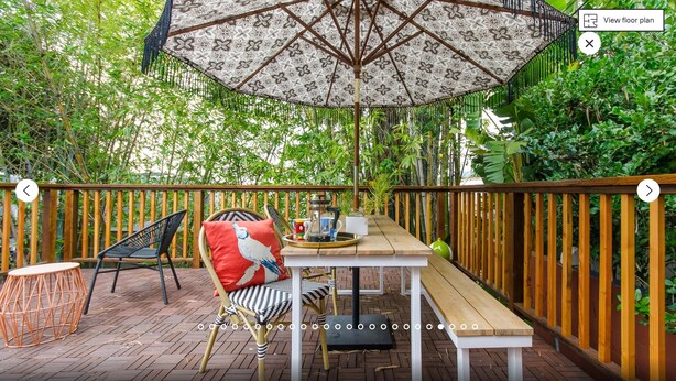 An outdoor patio with a wooden table, chairs, and a patterned umbrella.