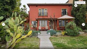 A red house with a balcony, a garden with cacti, and a pathway leading to the entrance.