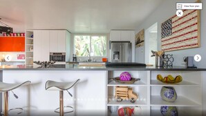 A modern kitchen with white cabinetry, a central island with bar stools, and decorative items on shelves.
