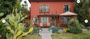 Una casa roja con balcón, un jardín con cactus y un camino que lleva a la entrada.