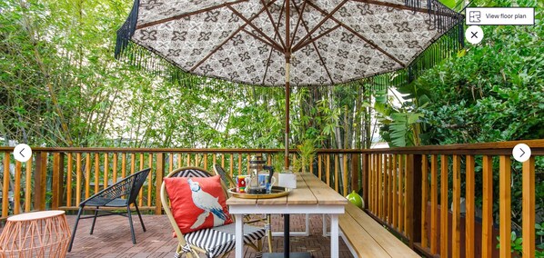 Un patio al aire libre con una mesa de madera, sillas y un paraguas estampado.