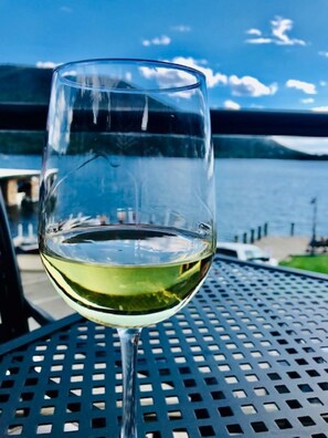 Et glas hvidvin på et metalbord med udsigt til vand og en bro i baggrunden.