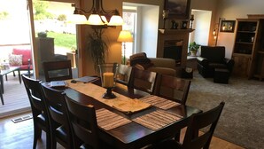 A dining area with a wooden table, chairs, and a chandelier. There is a fireplace with a mantel and a television in the background. - - Pikes Peak/Garden of the Gods!  Booking FAST! (Colorado Springs)