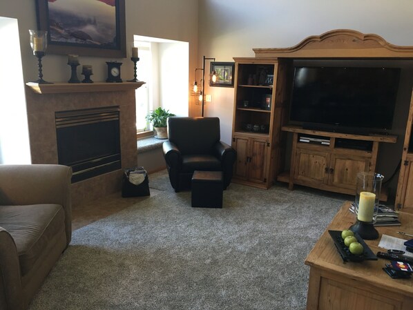 Una sala de estar con chimenea, televisor, sillón de cuero y mueble de entretenimiento de madera.