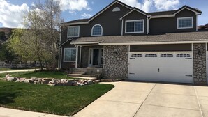 A two-story house with a stone facade, a garage with three doors, and a well-maintained lawn. - - Pikes Peak/Garden of the Gods!  Booking FAST! (Colorado Springs)