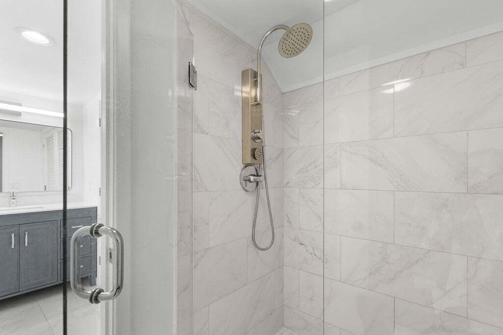 A modern bathroom with a glass shower enclosure, a handheld showerhead, and a wall-mounted control panel.