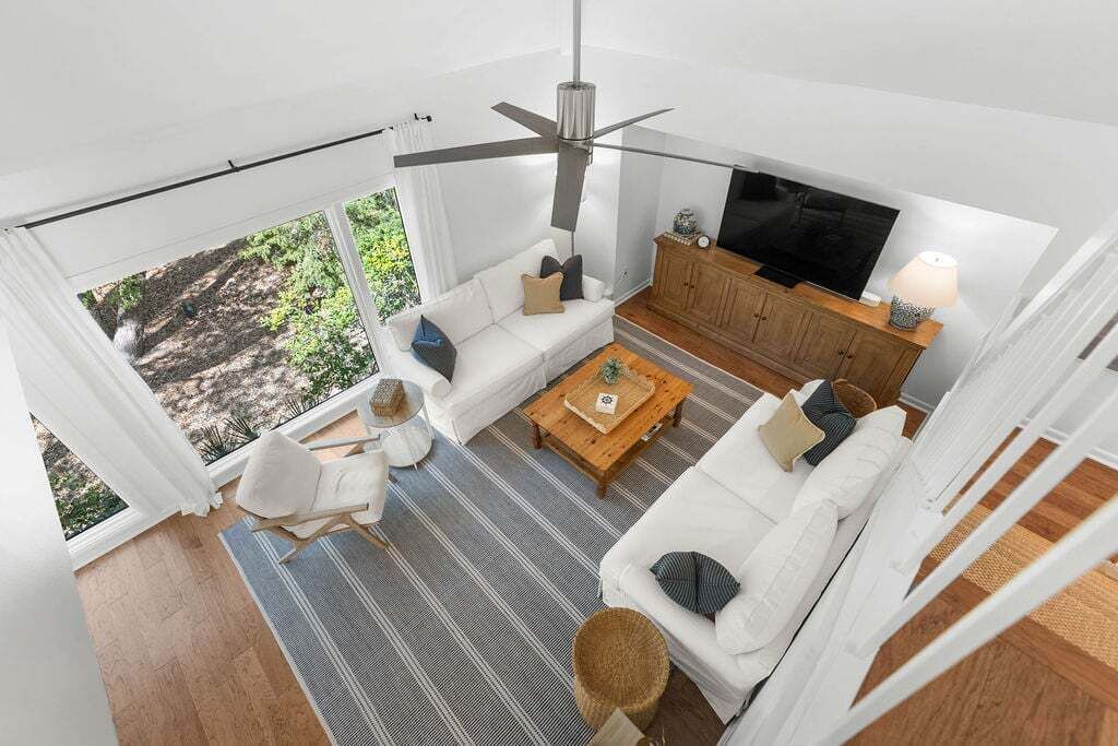 Una sala de estar moderna con ventilador de techo, sofás blancos, una mesa de centro de madera y un televisor.