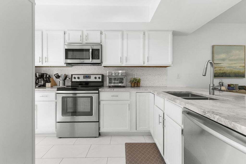 A modern kitchen with white cabinets, stainless steel appliances, a microwave, oven, and a sink.
