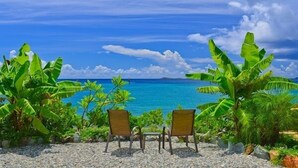 Blick auf einen Strand mit zwei Stühlen, die dem Meer zugewandt sind, umgeben von tropischer Vegetation.