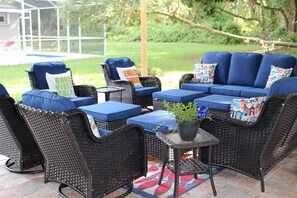An outdoor patio with wicker furniture, blue cushions, and a small table with a plant.