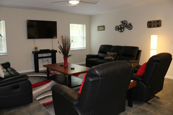 A living room with a flat-screen TV, a coffee table, and two black leather sofas.