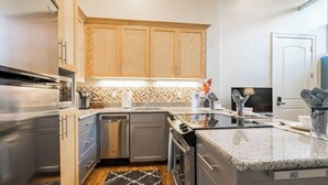 A modern kitchen with wooden cabinets, a stainless steel refrigerator, a dishwasher, and a granite countertop. - Unique Apartment in Downtown Provo (Unit #11) (Provo)