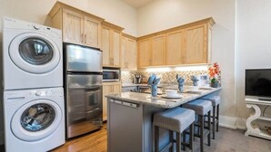 A compact kitchen with a washing machine, refrigerator, and a small island with bar stools. - Unique Apartment in Downtown Provo (Unit #11) (Provo)