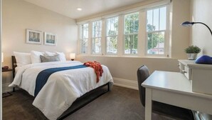A bedroom with a bed, bedside table, lamp, desk, chair, and a window with a view of trees and buildings. - Unique Apartment in Downtown Provo (Unit #11) (Provo)