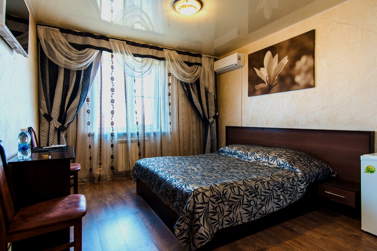 A bedroom with a bed, a desk, a chair, and a wall-mounted air conditioner.