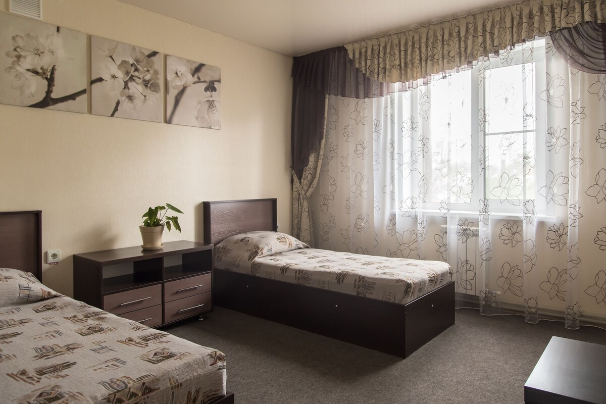 A bedroom with two beds, a nightstand, a dresser, and a window with floral curtains.