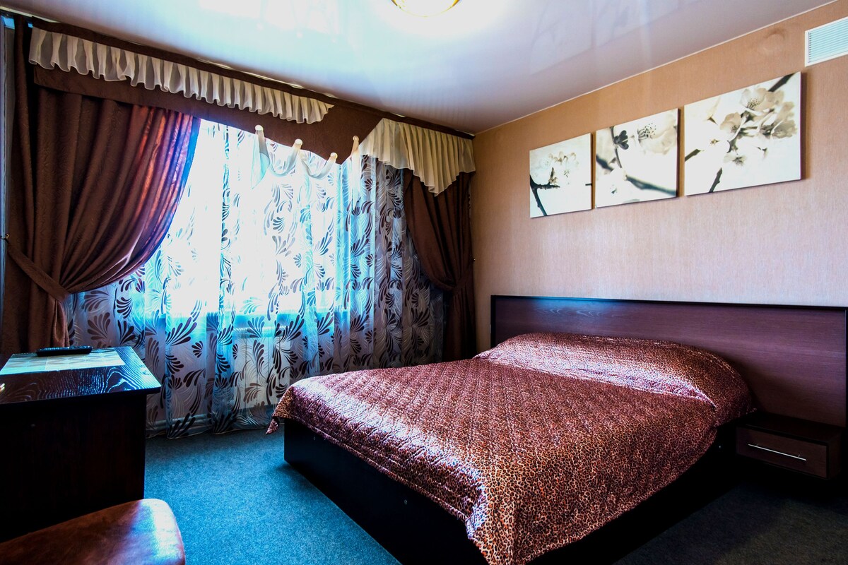 A bedroom with a bed, curtains, a desk, and wall art.