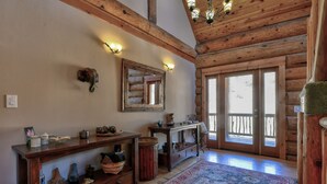A log cabin interior with a wooden bench, a mirror, a rug, and a wooden door leading outside.