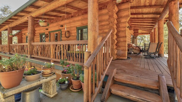A wooden log cabin with a covered porch, outdoor seating, and potted plants.