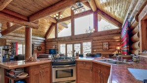 A log cabin kitchen with wooden cabinets, a stove, and a large window.