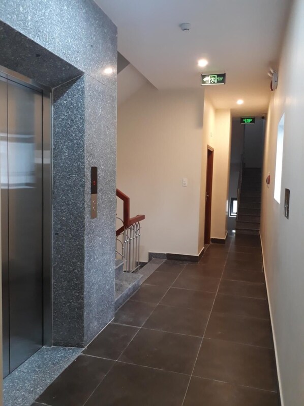 Un pasillo con pared de mármol, una escalera y una puerta con pantalla digital.