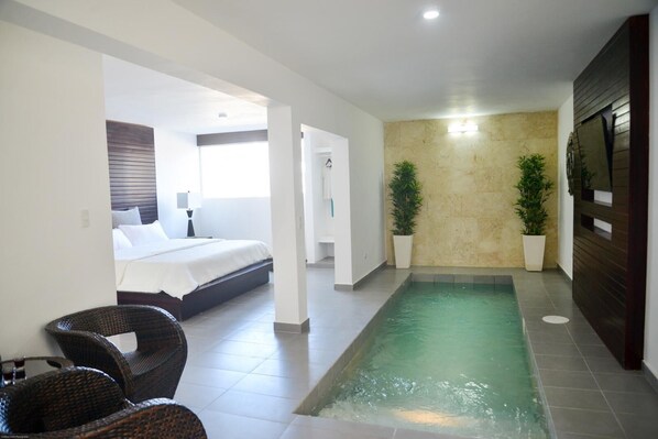 A modern hotel room with a bed, a small sitting area with wicker chairs, a built-in pool, and potted plants. - AHNVEE RESORT AND SPORTS (Sosúa)