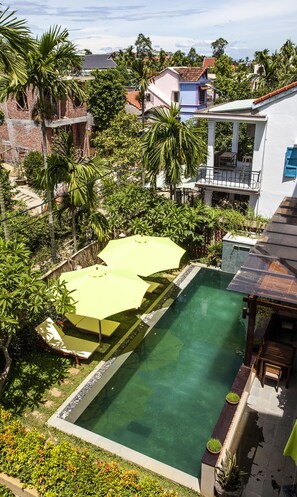 A swimming pool surrounded by lush greenery and a white building with a balcony. - Hoi An Silk River Villa (Da Nang)