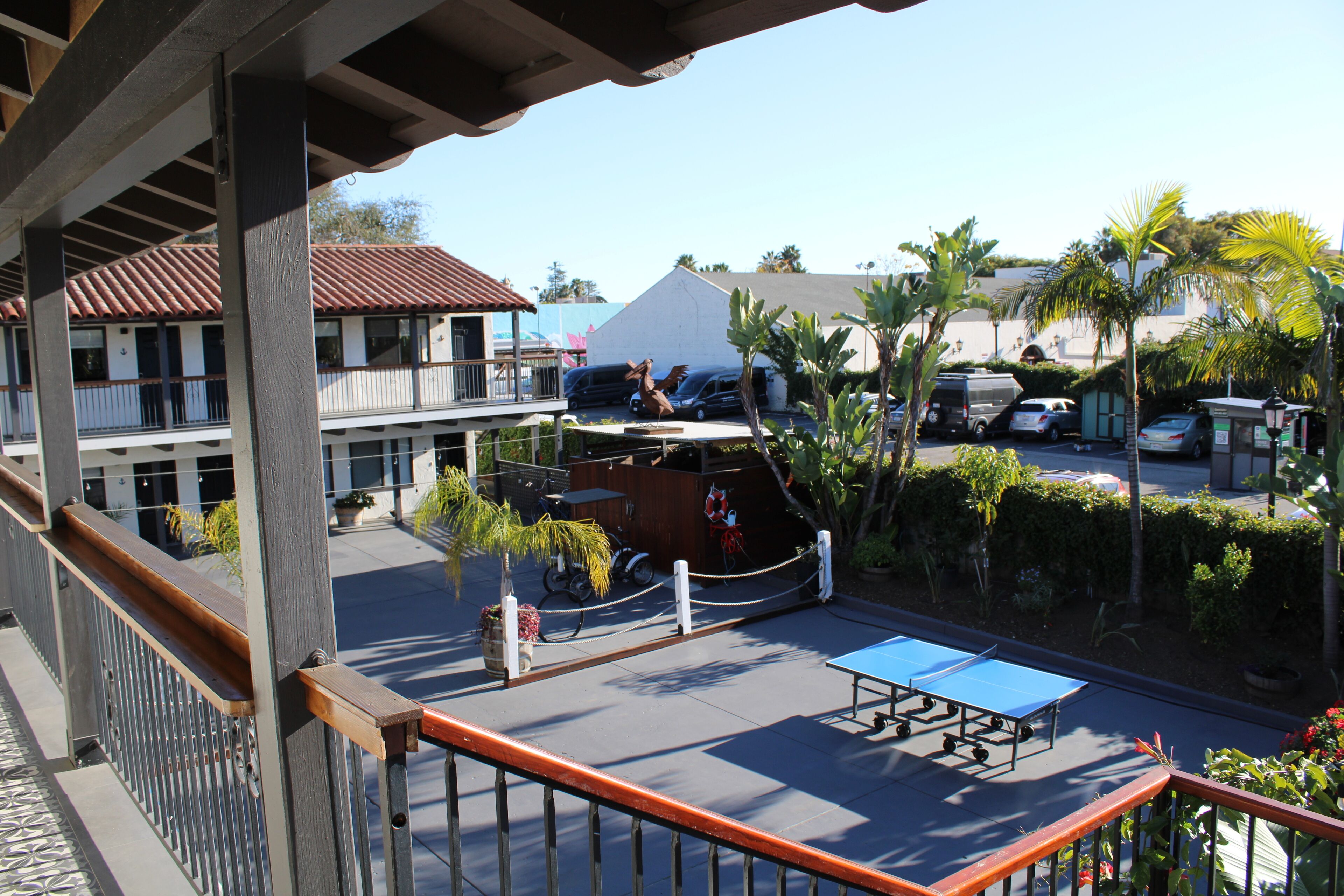 A balcony with a view of a parking area, a building with a red roof, and a blue table tennis table.