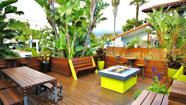 Une terrasse extérieure avec des tables et des bancs en bois, entourée d’une végétation tropicale luxuriante.