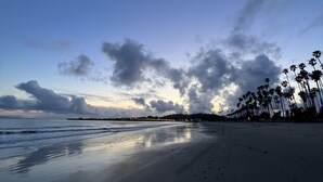Une plage bordée d’une mer calme, une lune en croissant et des palmiers à l’horizon.