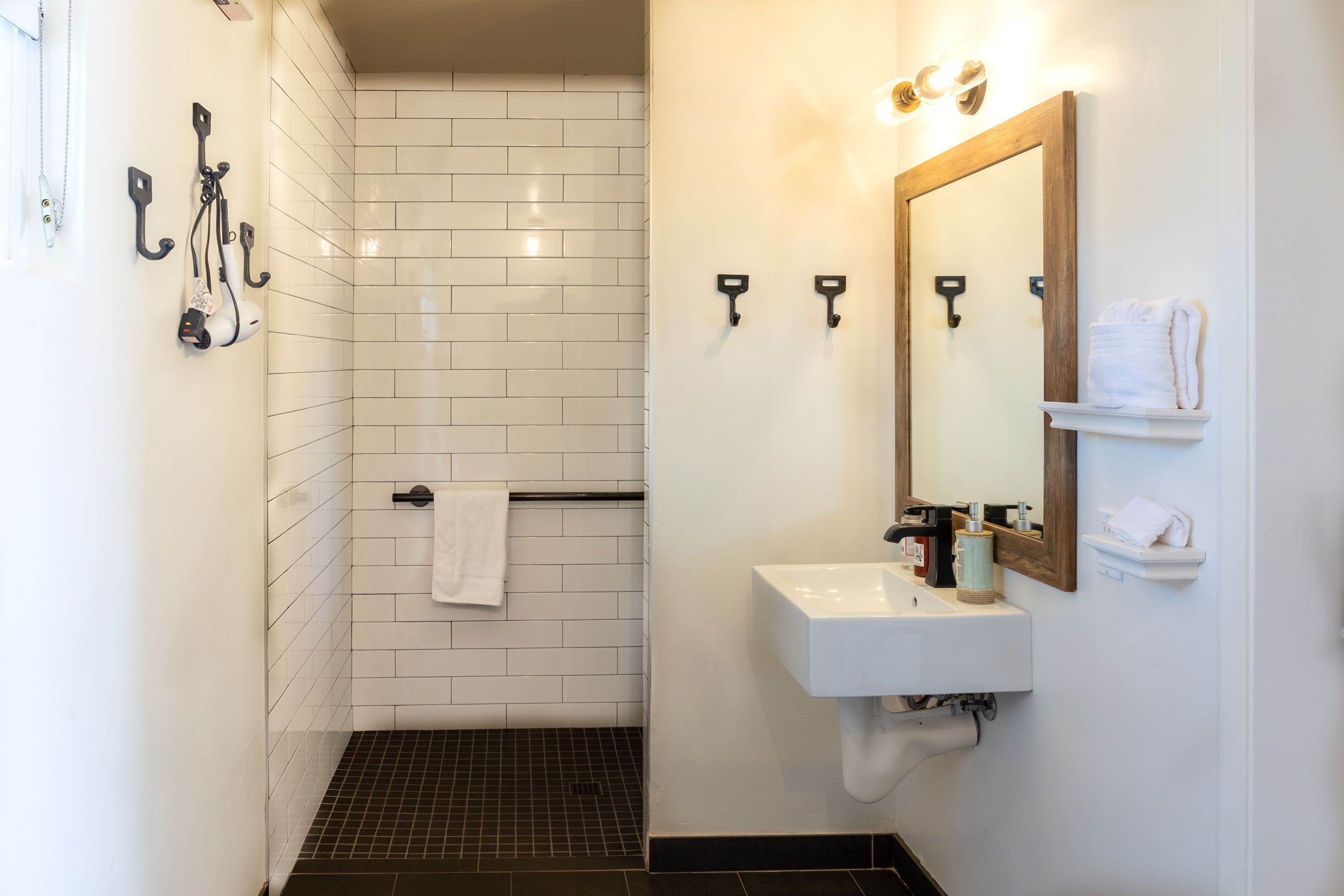 A modern bathroom with a white tiled shower, a sink with a mirror, and towel hooks.