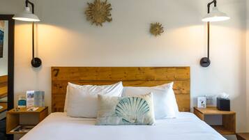 A hotel room with a wooden headboard, two white pillows, a decorative pillow with a fan design, two bedside tables with lamps, and wall art.