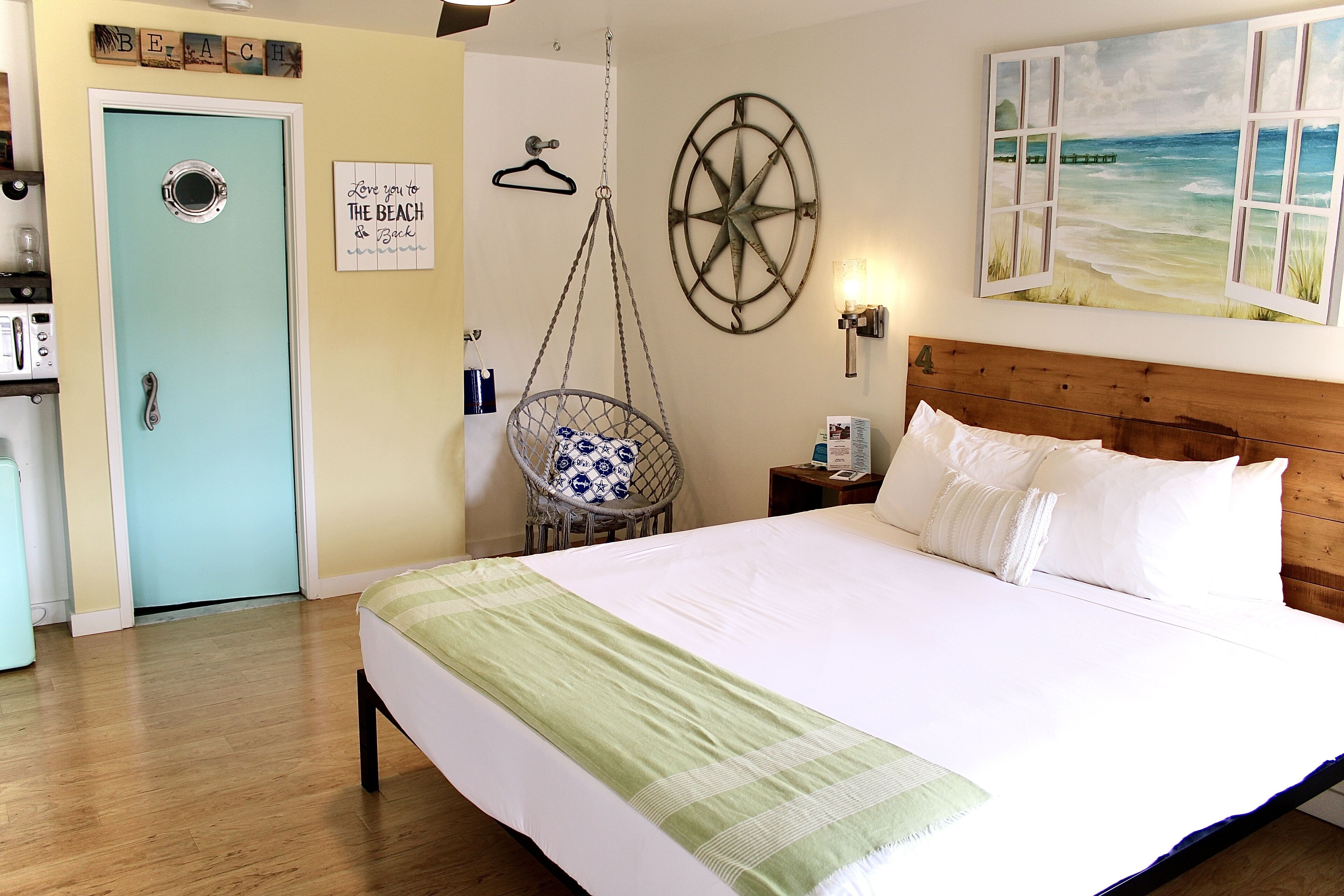 Un dormitorio con cama, una silla colgante, un reloj de pared, un cuadro de una playa y un letrero en la puerta.