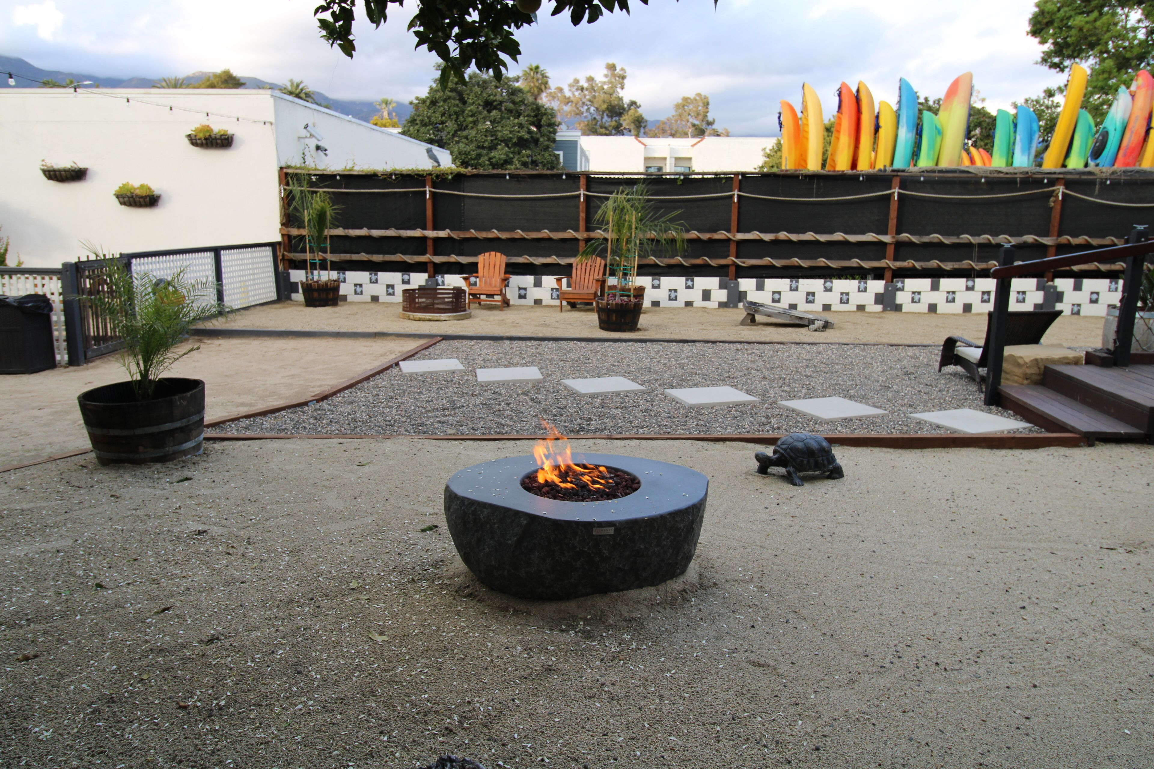 A courtyard with a fire pit, seating, and colorful kayaks in the background.