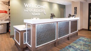 Mostrador de recepción con un letrero que dice "Welcome to the Golden State", una máquina de café y un quiosco digital.