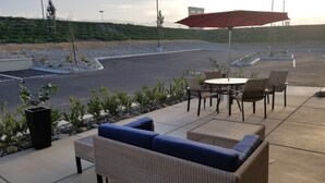 Un área de patio al aire libre con un sofá y sillas de mimbre, y un paraguas rojo.