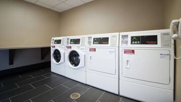A laundry room with four front-loading washing machines and dryers, a tiled floor, and a vented ceiling.