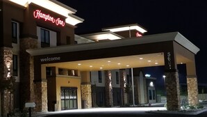 Entrada de un hotel Hampton Inn con un cartel de 'welcome', pilares de piedra y un corredor cubierto.