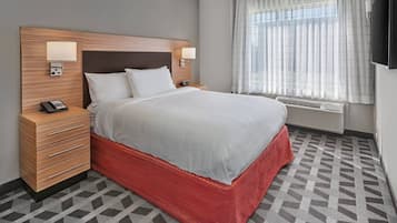 A hotel room with a bed, bedside tables, a telephone, a television, and a window with curtains.