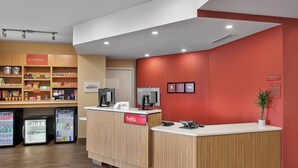 A hotel reception area with a wooden reception desk, a 'hello' sign, a 'In a Pinch' shelf with snacks, a 'Marriott Bonvoy' sign, and a 'Managed on Duty' sign. - TownePlace Suites by Marriott Edmonton Sherwood Park (Sherwood Park)