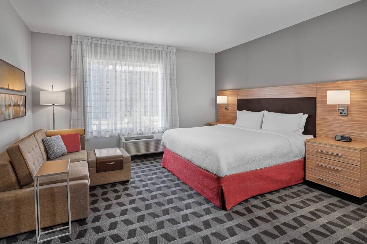 A hotel room with a bed, a sofa, a nightstand, and a lamp.
