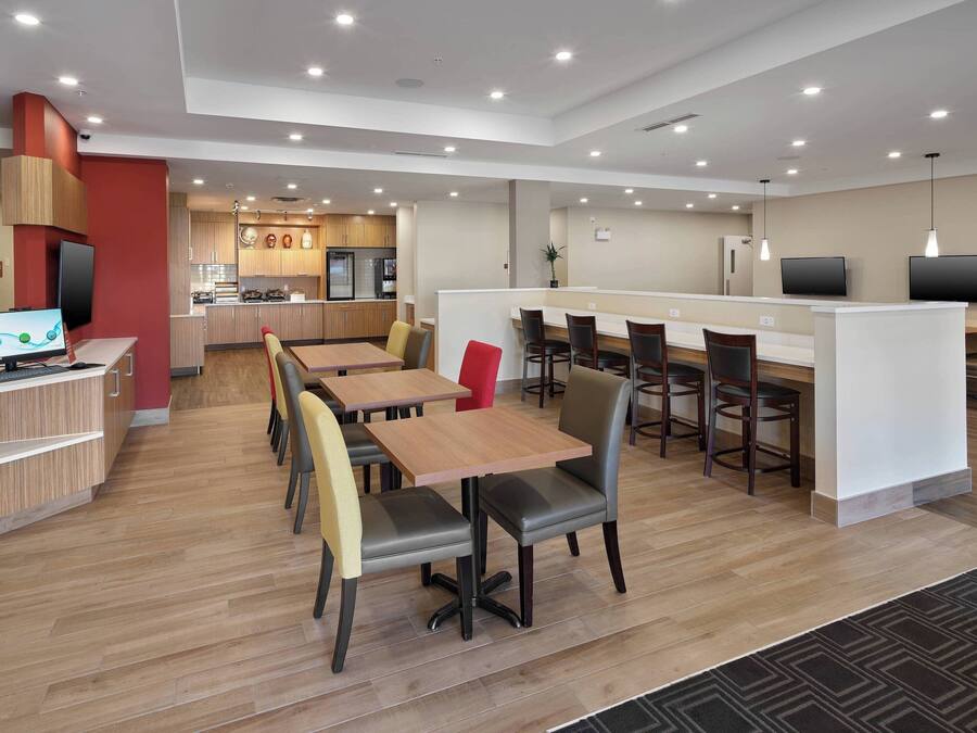 Un área de comedor moderna con varias mesas y sillas, una cocina al fondo y un mostrador de recepción con una computadora.