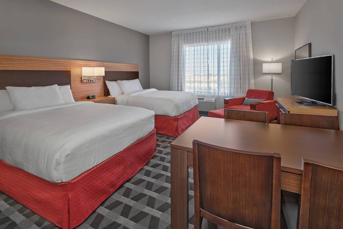 A hotel room with two beds, a TV, a desk, and a chair.