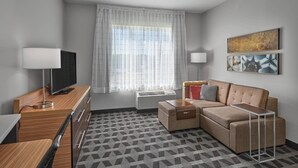 A modern hotel room with a sofa, a TV, a desk, and a patterned rug. - TownePlace Suites by Marriott Edmonton Sherwood Park (Sherwood Park)