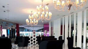Un hall d’entrée spacieux, doté de chaises noires au design moderne, d’un grand lustre et d’un mur décoratif central.