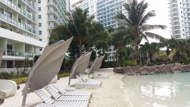 Un complexe hôtelier doté d’un espace piscine agrémenté de chaises longues et de parasols, entouré de palmiers et bordé d’une côte rocheuse.